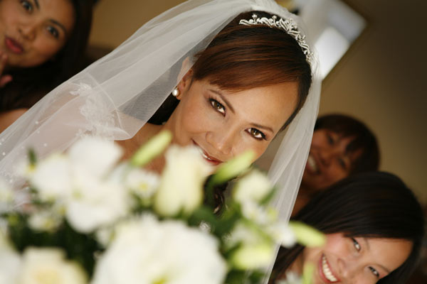 Magazine style fashion photoshoot in Orange County. Portrait of the Bride in her wedding dress looking at her bouquet of flowers with brides maids in the background.