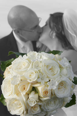 Magazine style fashion photoshoot in Santa Barbara. Portrait of the Bride and Groom after the ceremony. This shot shows a kiss with the bouquet of flowers out in front. The bride is in her wedding dress with veil and bouquet.