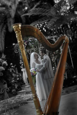 Magazine style fashion photoshoot in Santa Barbara. Portrait of the Bride and Groom photographed through the harp. This shot shows the bride with the bouquet of flowers and the groom in a gray tuxedo.