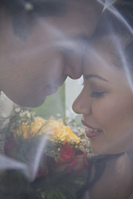 Magazine style fashion photoshoot in Santa Barbara. Portrait of the Bride and Groom photographed through the brides veil. This is a close up headshot with the bouquet of flowers between the couple.